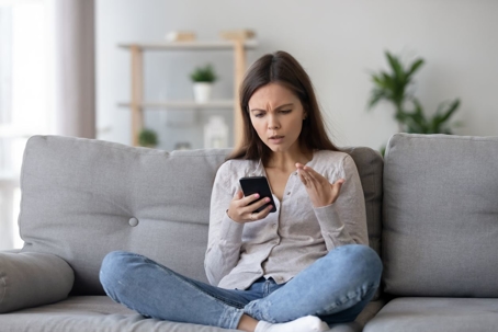 Confused woman with cellphone sitting on couch
